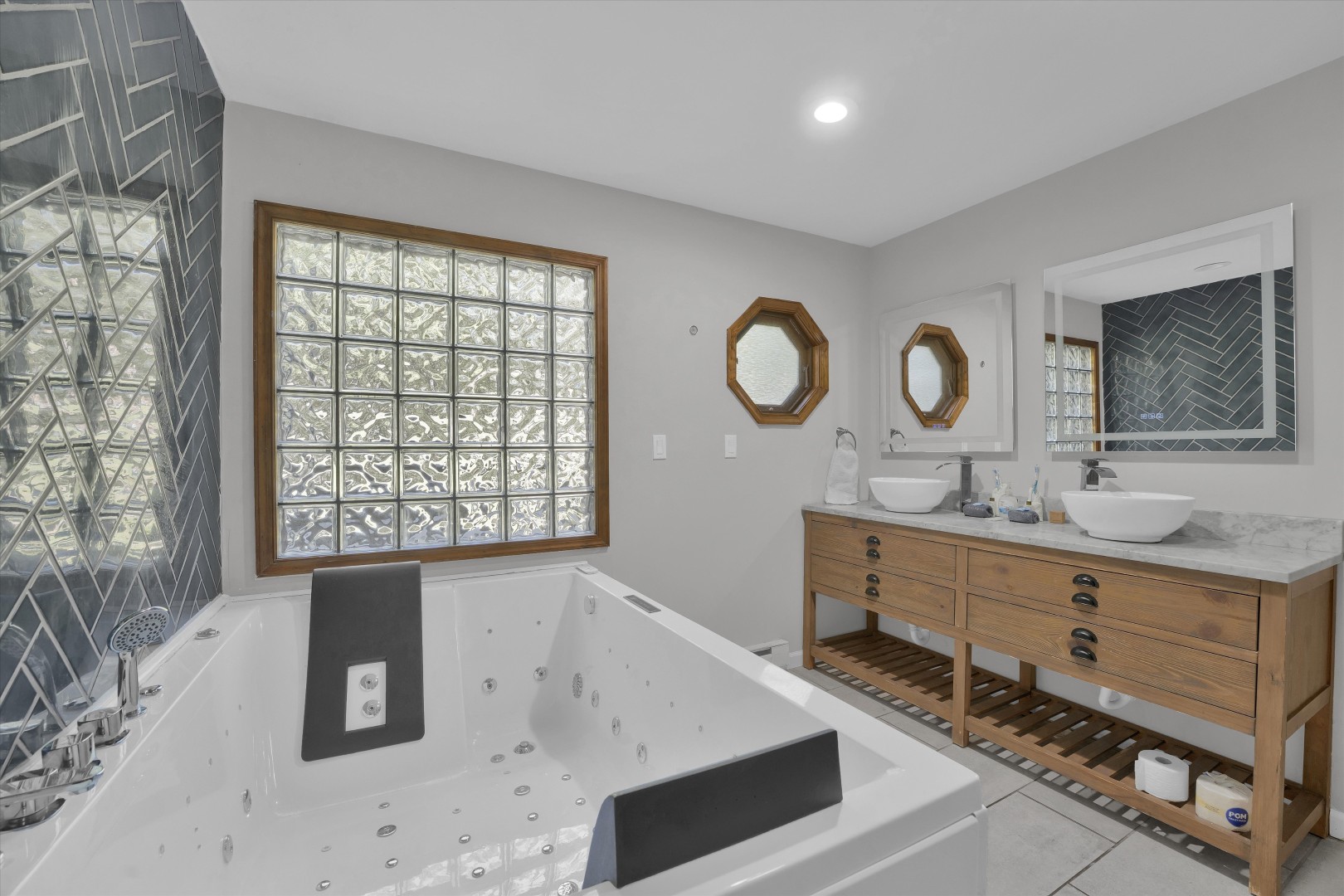 Indulge in a spa-like retreat in the primary suite bathroom, featuring a deep Jacuzzi soaking tub, dual vanities, and ambient lighted mirrors.