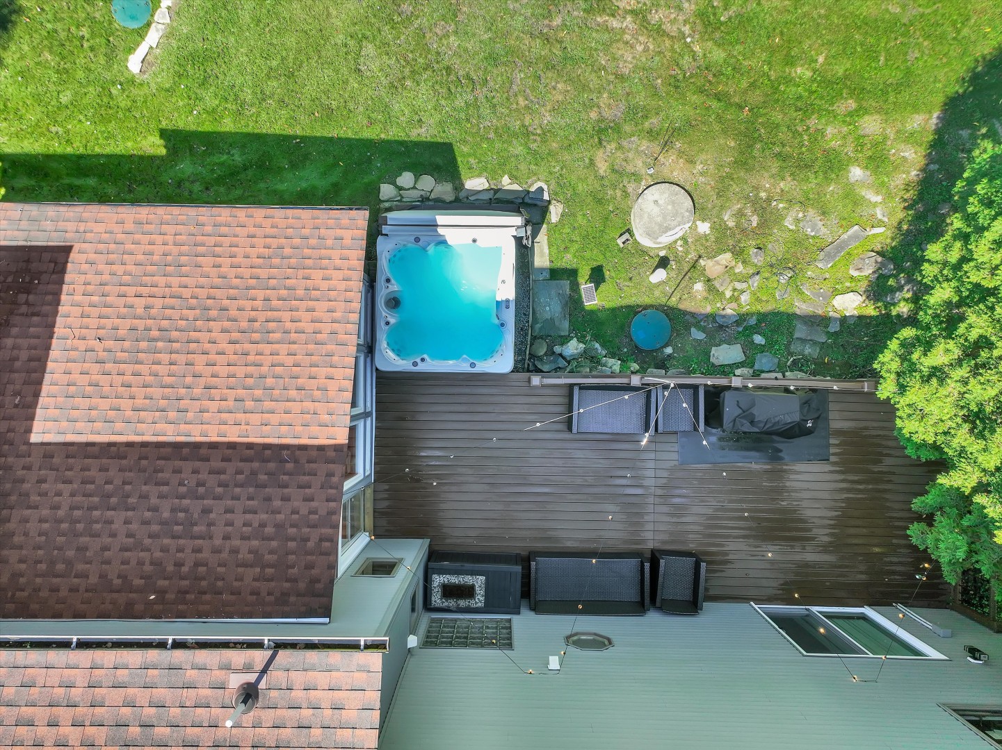 Bird’s-eye view of the expansive back deck, complete with a private hot tub, patio seating, and forest views.
