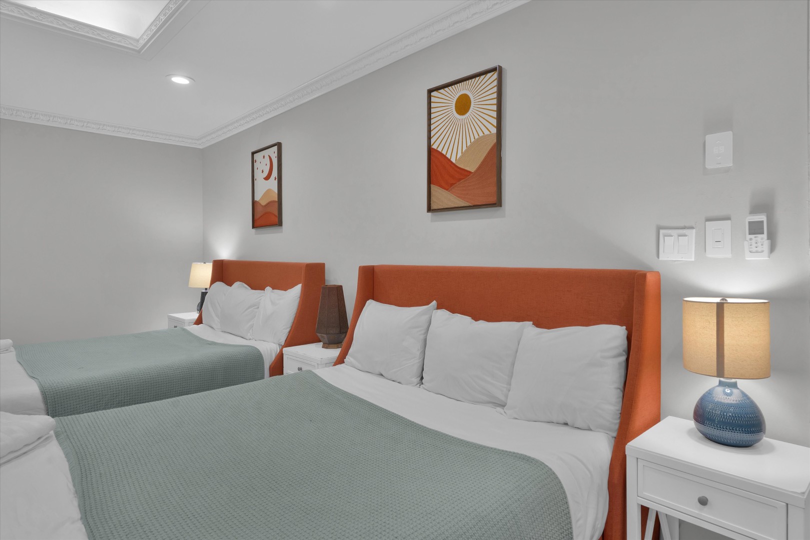 Vibrant group bedroom featuring two queen beds with burnt-orange headboards, plush pillows, and crisp white linens.